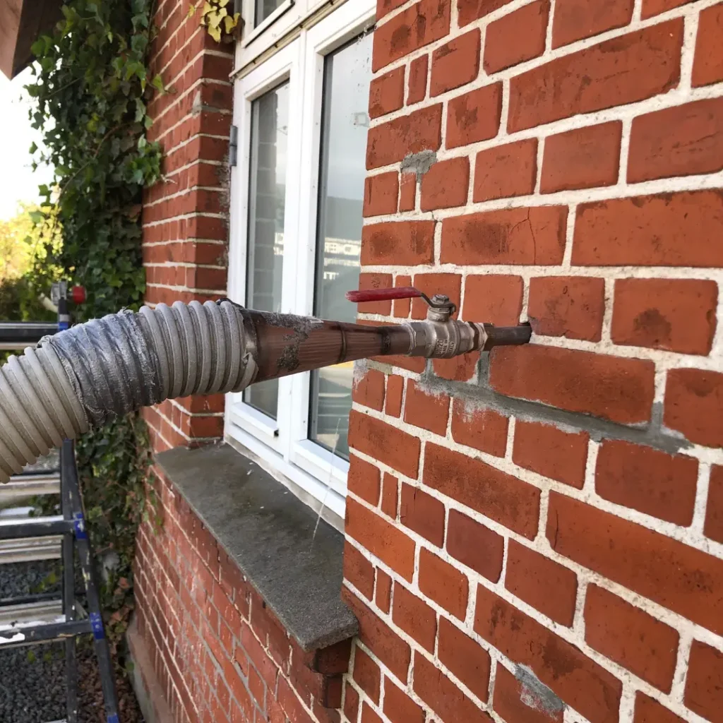 Slange til indblæsning af isolering ført ind gennem en fuge i en murstensfacade