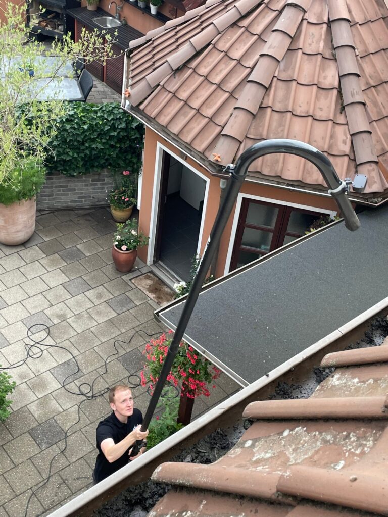 Medarbejder renser tagrenden fra jorden med en lang sugestang